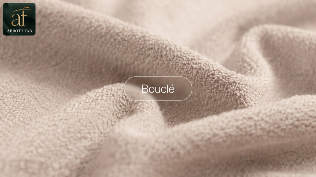 ABBOTT FAB product showcase image featuring the Abbott Fab brand logo, a centered badge reading Bouclé, and a close-up photograph of beige boucle fabric in soft, textured loops and folds.